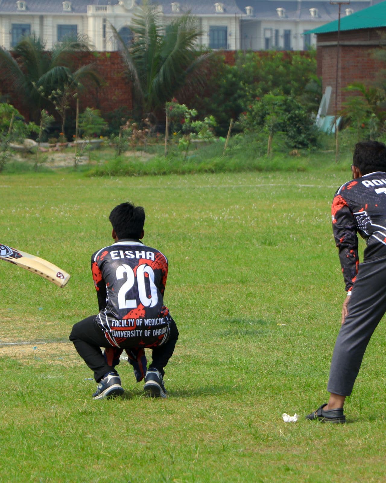 Community cricket match in progress on a grass ground as a batsman faces the bowler